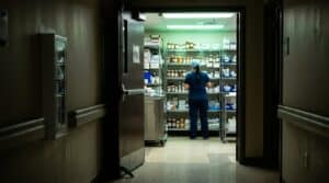 Nurse in scrubs at the shelves of a hospital medication supply room seen from the corridor, representing a nurse arrested for theft in Texas